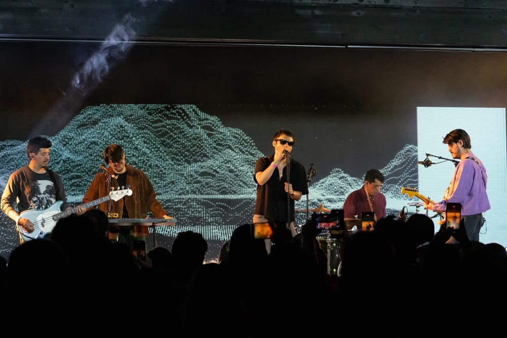 Odisseo performing live on stage during their debut U.S. tour in Chicago, with band members playing instruments under a digital backdrop.